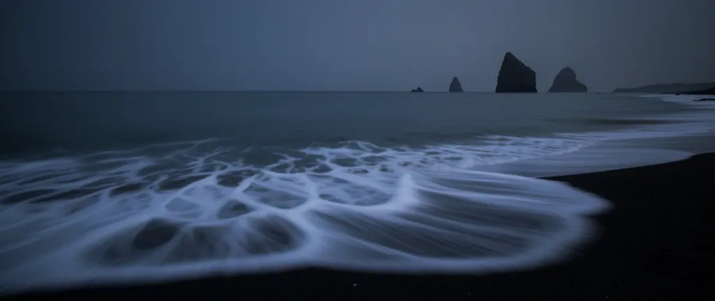 A black sand beach with long-exposure white waves ultrawide